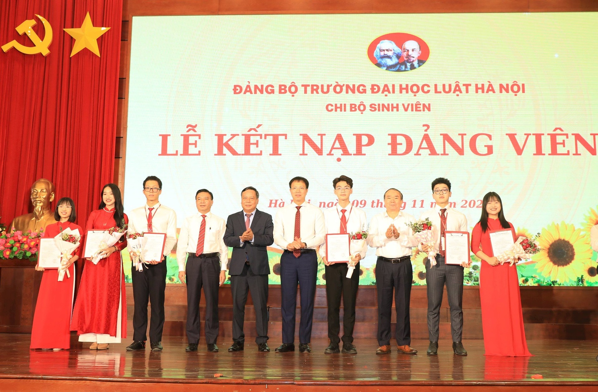 Phó Bí thư Thành ủy Nguyễn Văn Phong cùng các đồng chí lãnh đạo Đảng bộ Trường Đại học Luật Hà Nội trao quyết định và tặng hoa chúc mừng các đảng viên mới.
